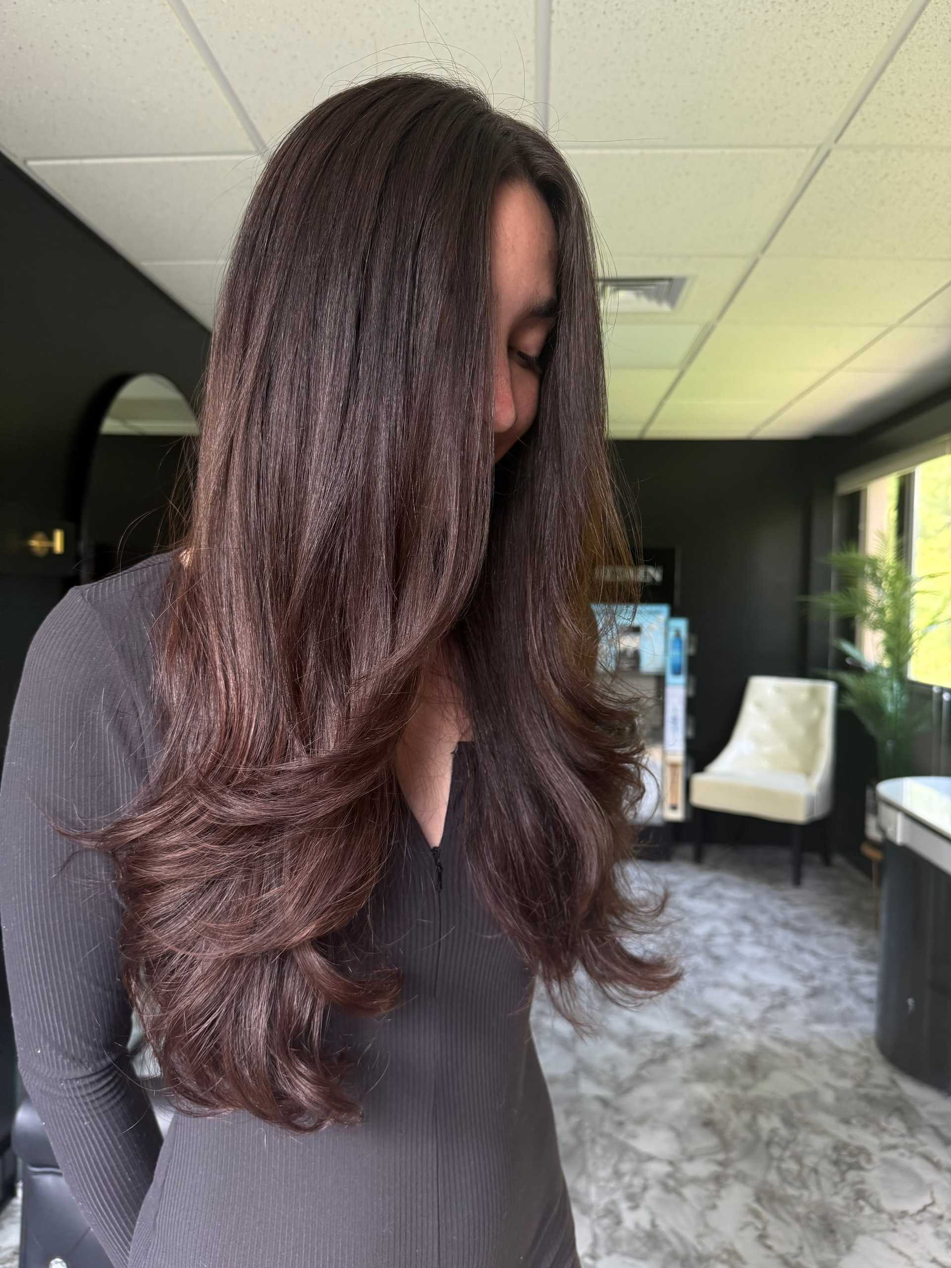 Woman with long, wavy brown hair in modern black and white interior setting.
