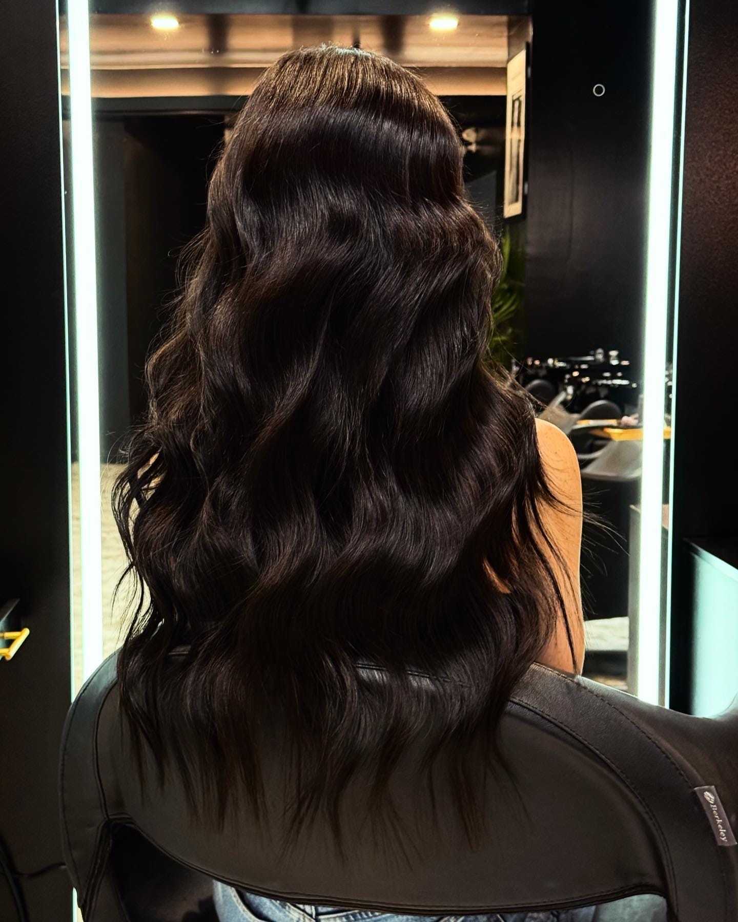 Long, wavy dark hair styled elegantly in a salon setting.