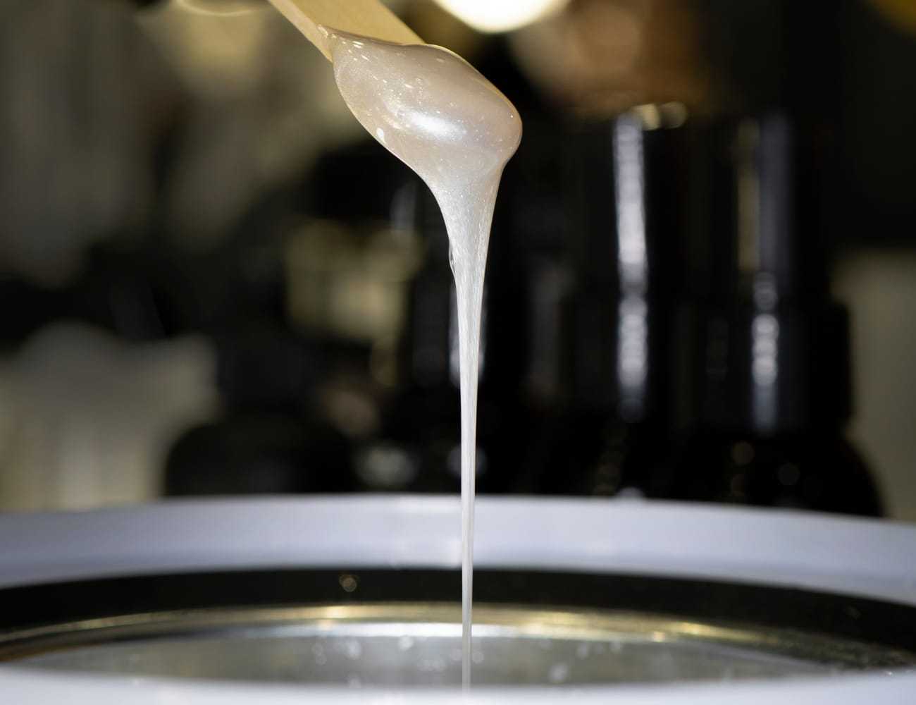 Hot wax melting in a pot, with a wooden spatula lifting a stream of wax.